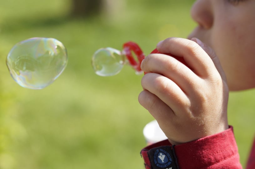 A child is blowing soap bubbles in the air through a bubble wand.