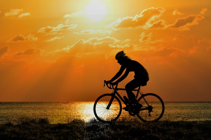 Cyclist riding beside a lake against the background of the setting sun